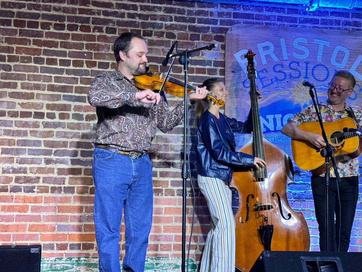 Alex Leach smiles while playing guitar next to fiddle and upright bass at Bristol Sessions Nights: Mountain Songs, Bristol Listening Room, L.C. King Building, Bristol, Tennessee