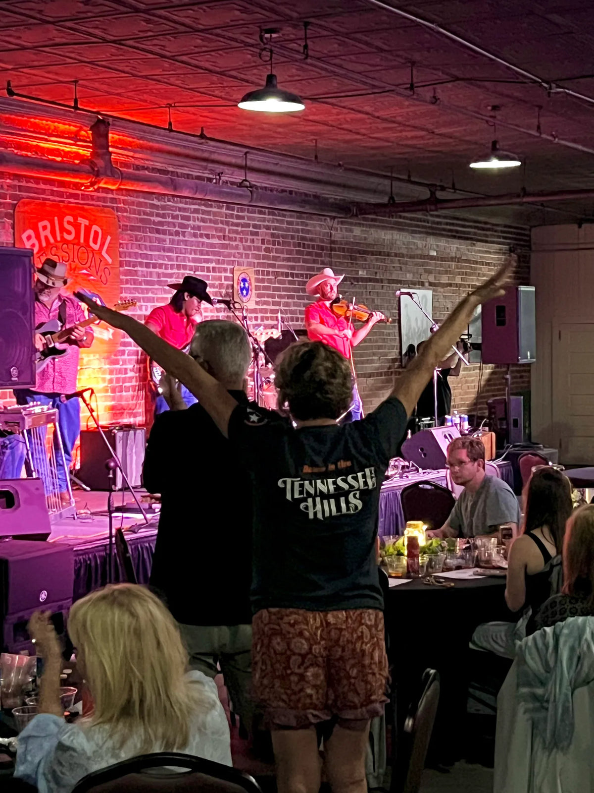 A guest in a Tennessee Hills shirt throws her arms up as the band plays at Bristol Sessions Nights: A True Taste of Tennessee, Bristol Listening Room, L.C. King Building, Bristol, Tennessee